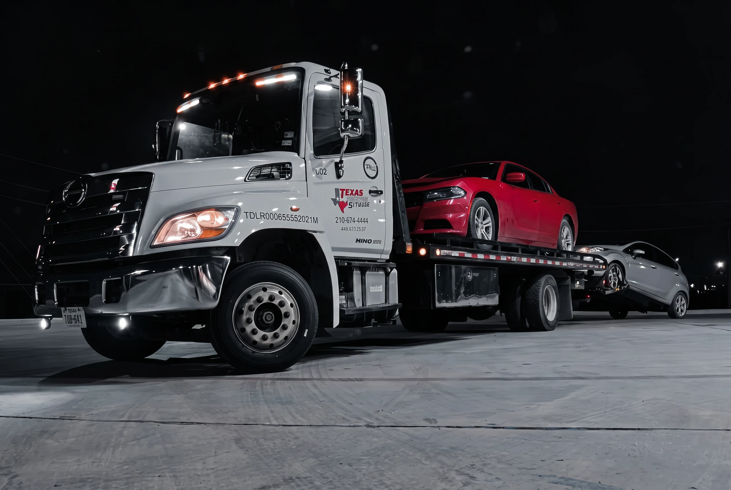 Texas Roadside Services flatbed truck at night carrying a red Dodge Charger